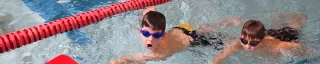 Two kids in the pool holding on to kickboards